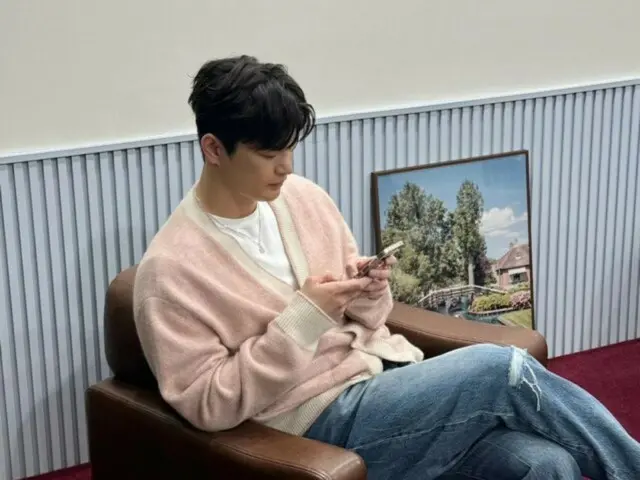 穿著粉紅色開襟衫的徐仁國看起來很放鬆……不知道他在智慧型手機上看什麼？